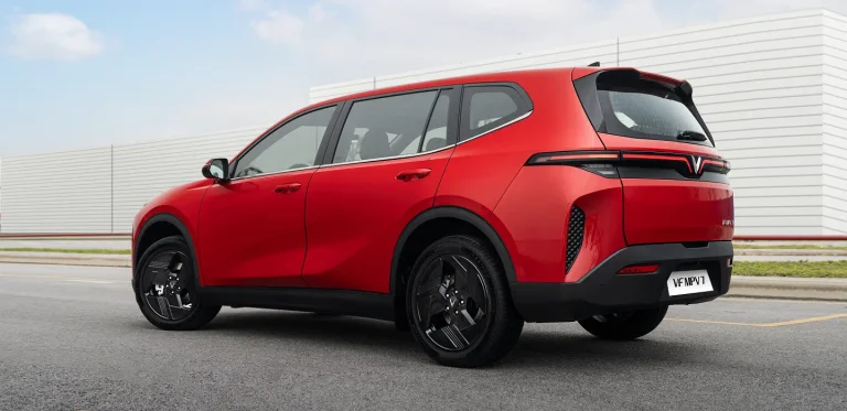 VinFast MPV7 màu đỏ nhìn từ phía sau bên trái, đỗ trên bãi xe ngoài trời