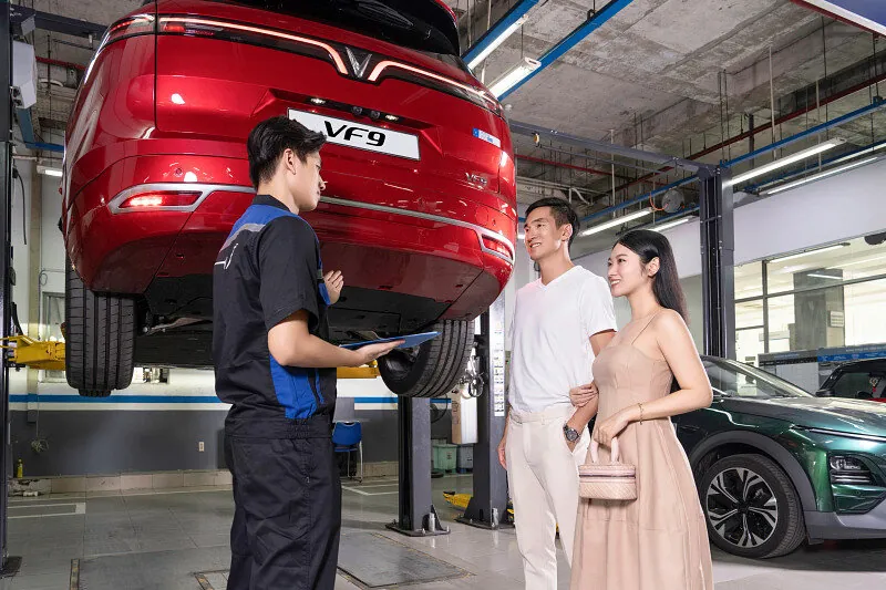 Cố vấn dịch vụ trao đổi với chủ xe bên cạnh chiếc VF 9 đang nâng trên cầu trong xưởng