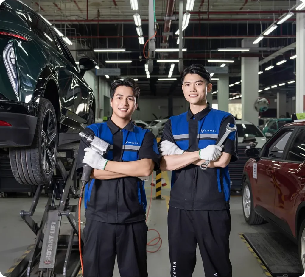 Hai kỹ thuật viên VinFast trong xưởng, phía sau là xe ô tô điện nâng trên cầu